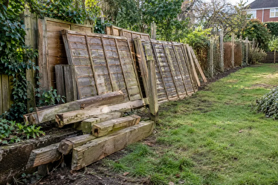 Old fence panels and rotten posts removed along a garden boundary