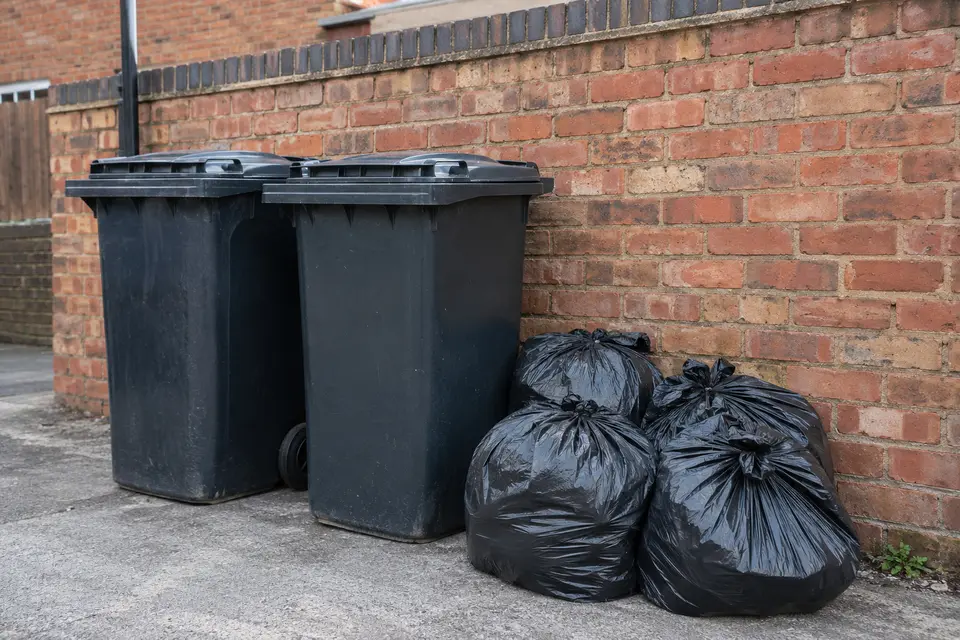 Overflowing wheelie bins and black sacks against a brick wall