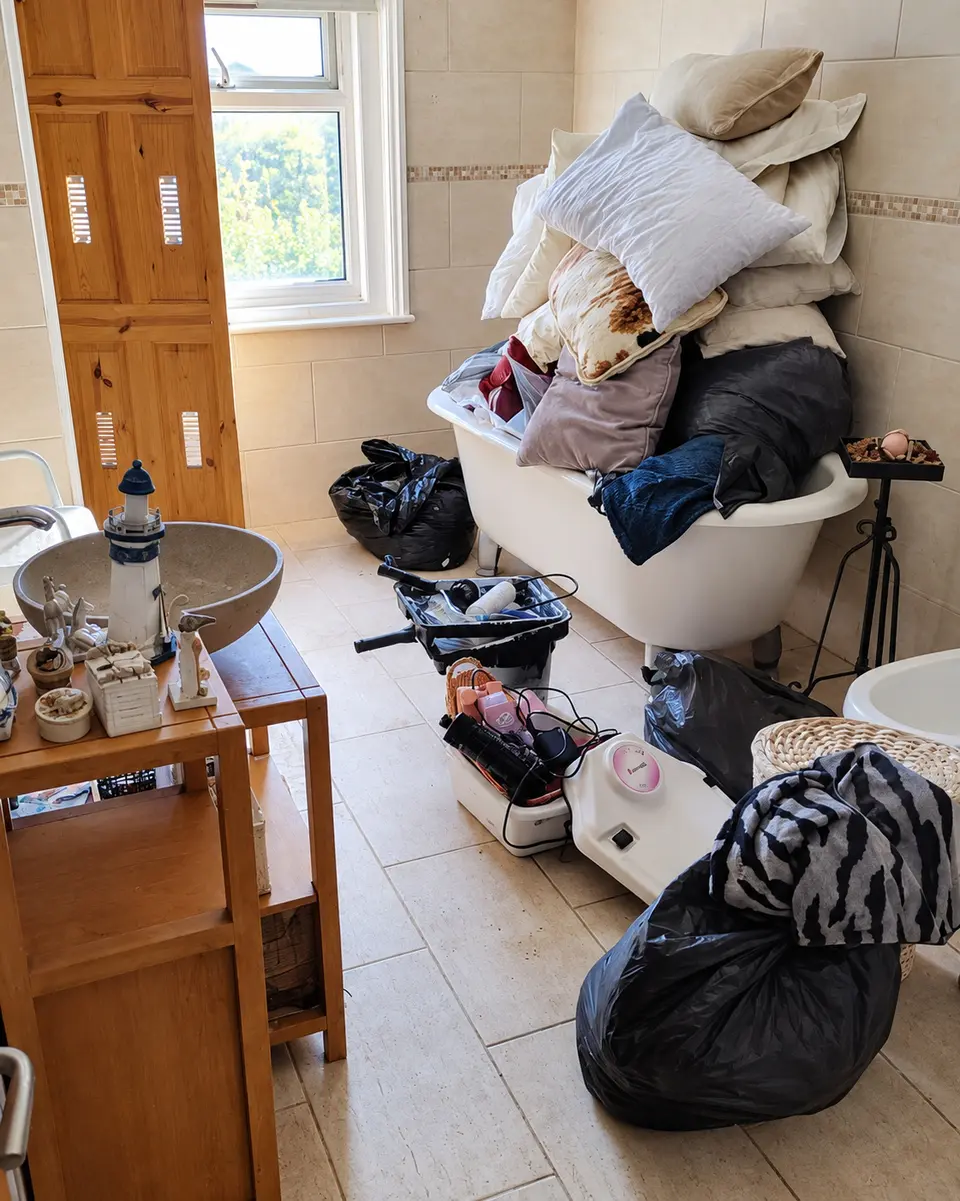 Before: a bathroom filled with bags, bedding and furniture during a house clearance