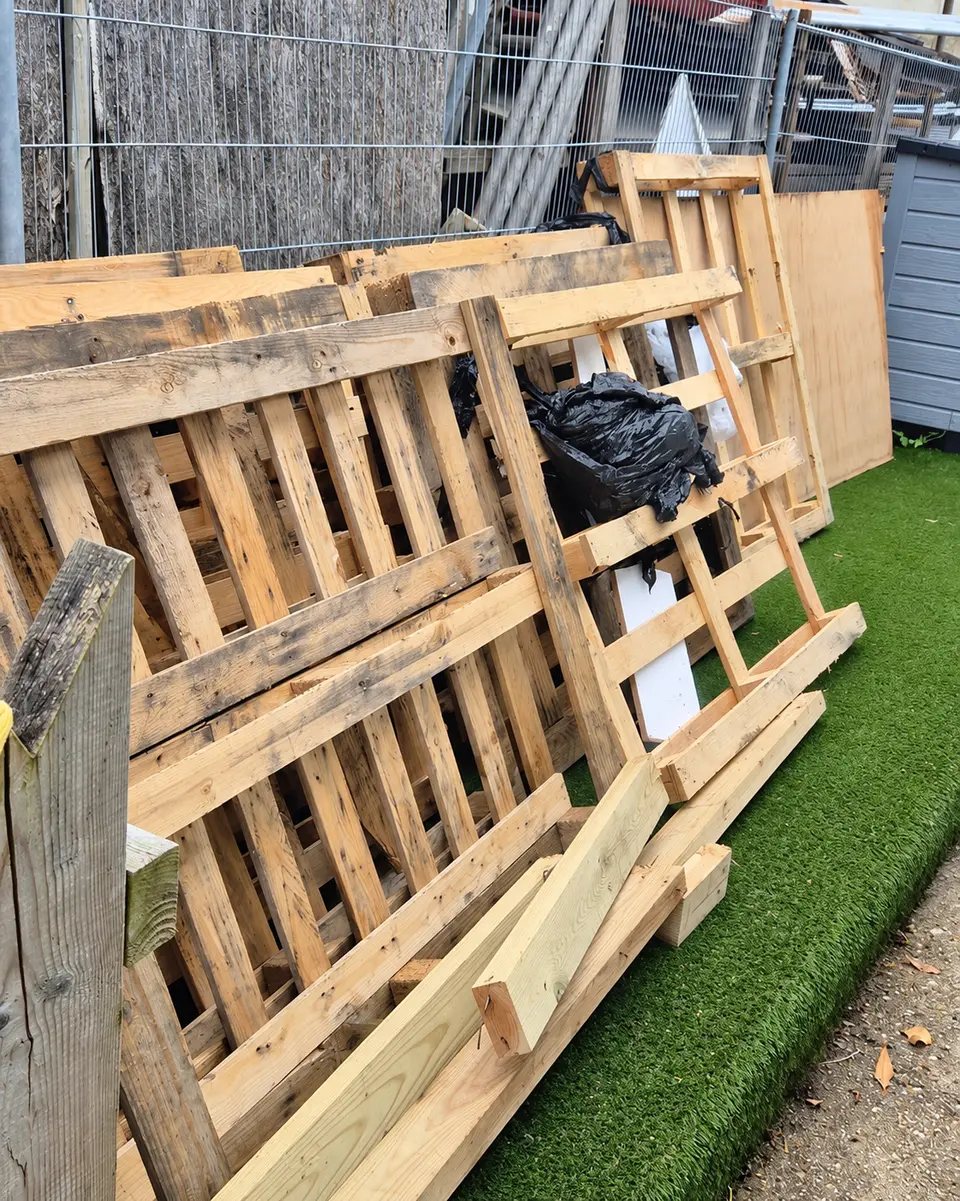 Before: old timber pallets and boards stacked on artificial grass