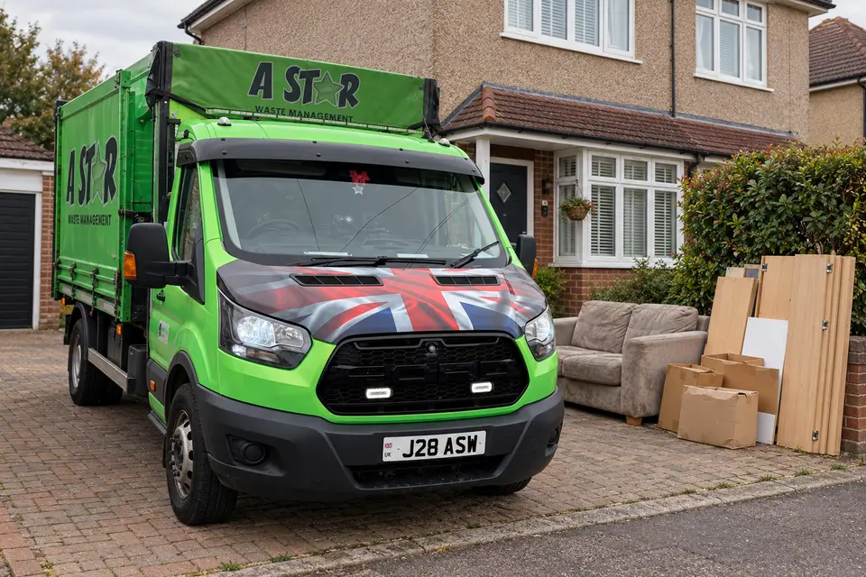 A Star Waste Management tipper van on a driveway beside an old sofa and flat-pack boards waiting for a house clearance